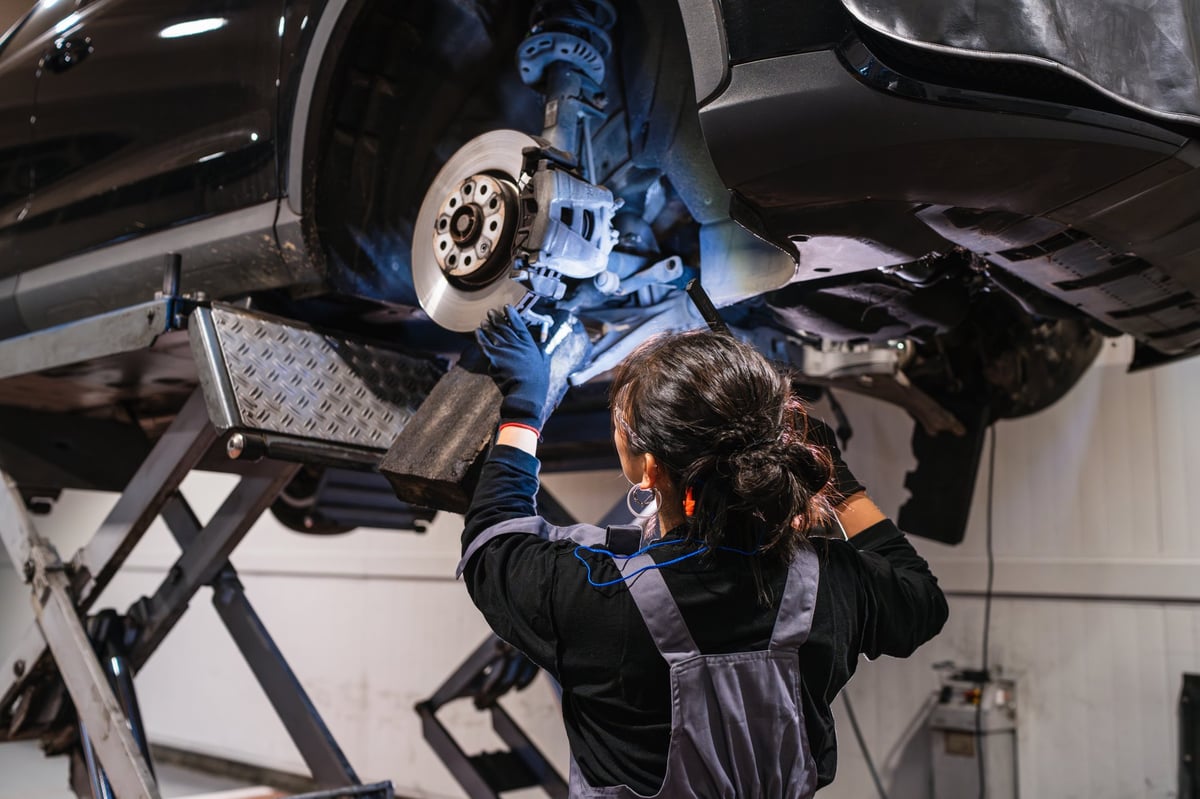 Mechanic working under a car on a hydraulic lift inspecting brakes