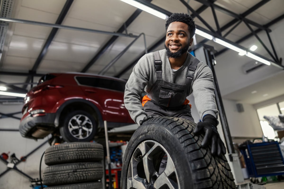 Smiling car technician rolling a tyre at the service centre